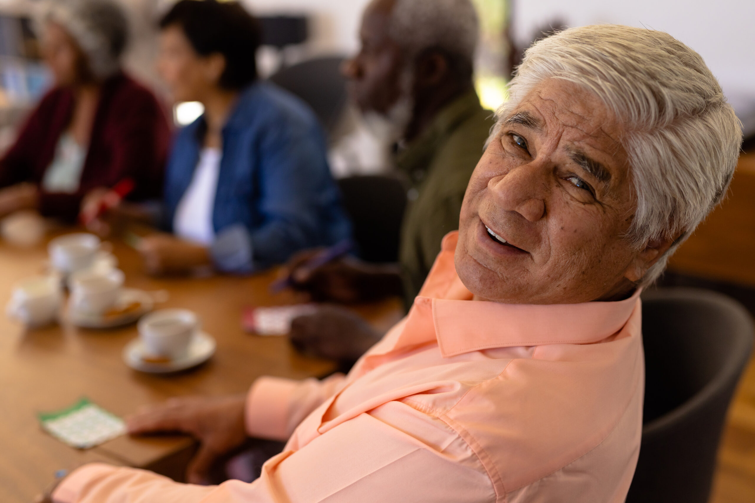 Portrait of smiling biracial senior man playing bingo with multiracial friends in nursing home. Coffee, happy, luck, leisure game, unaltered, togetherness, support, assisted living and retirement. Reforma a la Ley Integral de Protección al Adulto Mayor y Jubilados